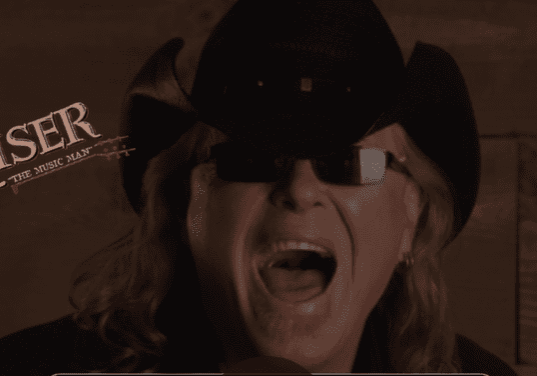 Person wearing a black hat and sunglasses, mouth open in surprise or excitement.